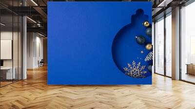 A creative Christmas design featuring an ornament-shaped cutout of Christmas ball filled with festive decorations and golden snowflakes on a dark blue background Wall mural