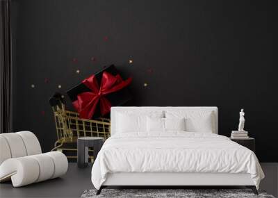 A small shopping cart holds a gift with a red ribbon on a dark background, symbolizing Black Friday or holiday shopping Wall mural