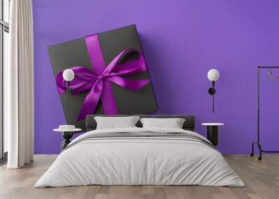 Above photo of black giftbox with ribbon wrapped as bow isolated on the violet background Wall mural