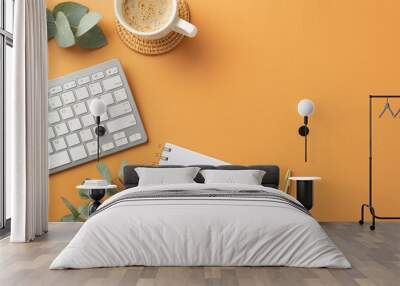 Business concept. Top view photo of workplace white keyboard organizer gold pen clips cup of coffee on rattan serving mat and eucalyptus leaves on isolated orange background with copyspace Wall mural