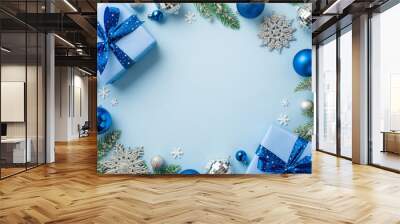 Christmas concept. Top view photo of blue silver baubles disco balls snowflake ornaments present boxes with bows pine branches confetti on isolated light blue background with empty space in the middle Wall mural