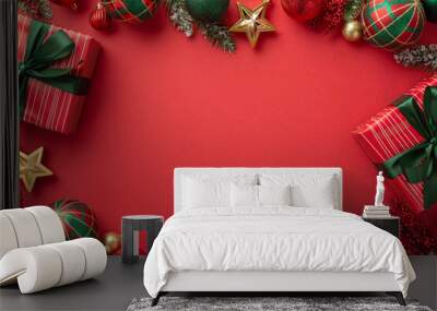 Christmas Eve concept. Top view photo of present boxes with bows red green baubles gold star ornaments mistletoe and pine branches in snow on isolated red background with blank space in the middle Wall mural