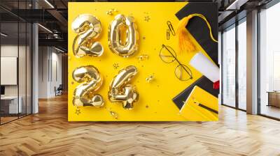 Commemorate graduation with a top-view photograph displaying 2024 gold balloons, a graduation cap, diploma, stationery, books, pencils, glasses, confetti on yellow background. Excellent for advert Wall mural