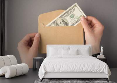 First person top view photo of female hands holding open craft paper envelope with hundred dollars banknote on isolated grey background with copyspace Wall mural