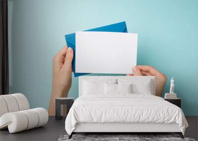 First person top view photo of hands holding blue envelope and white card on isolated pastel blue background with empty space Wall mural