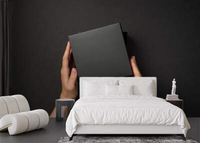 First person top view photo of hands holding open lid on black giftbox on isolated black background with empty space Wall mural