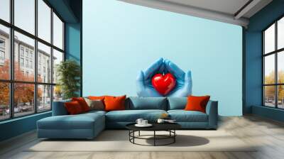 Heart disease defense strategy with this captivating birds-eye top scene displaying gloved hands cradling a heart on pale blue background with copy-space available for text or promotional use Wall mural