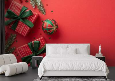 New Year celebration concept. Top view photo of red gift boxes with green ribbon bows baubles confetti mistletoe berries and pine branches in snow on isolated red background with blank space Wall mural