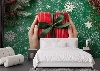 New Year concept. First person top view photo of female hands giving red present box with ribbon bow snowflake ornaments snow mistletoe berries and pine branches in frost on isolated green background Wall mural