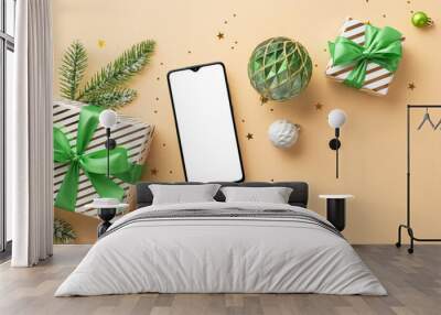 New Year concept. Top view photo of smartphone white and green baubles gift boxes pine branch in hoarfrost and confetti on isolated beige background with copyspace Wall mural