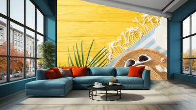 Sunny day essentials: top view of straw hat, sunglasses, slippers, beach blanket, palm leaf, shells, and starfishes on a vibrant yellow table Wall mural