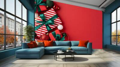 Top view of Christmas presents with green ribbons and holiday decorations on a vibrant red background Wall mural