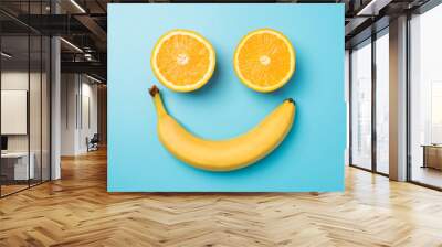 Top view photo of smiling face made from two orange halves and yellow banana on isolated pastel blue background Wall mural