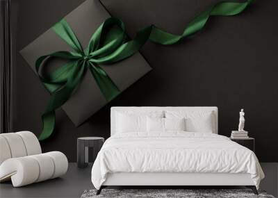 Top view photo of stylish black giftbox with green satin ribbon bow on isolated black background with empty space Wall mural