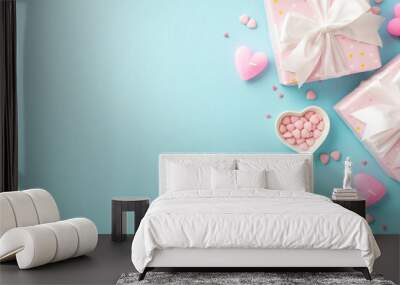 Valentine's Day concept. Top view photo of light pink gift boxes with white ribbon bows candles and heart shaped saucer with sprinkles on isolated pastel blue background with empty space Wall mural