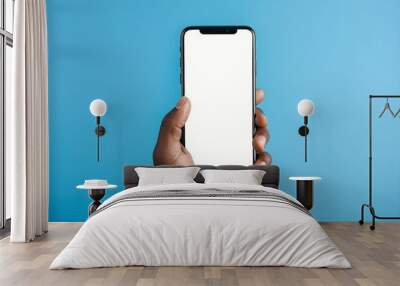 Black man's hand holding smartphone with blank screen with copy space, isolated on a blue background Wall mural