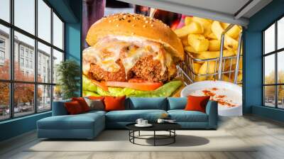 A chicken parma burger with lettuce and tomato on a white plate with french fries in a wire basket and dipping sauce
 Wall mural