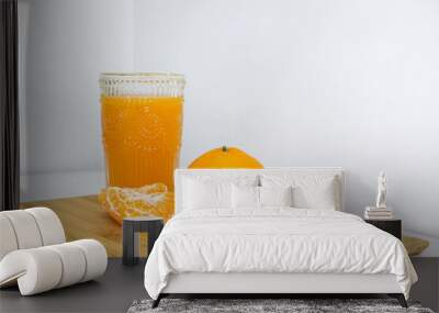 Glass of sweet and natural Mandarin orange juice, full of vitamin and nutritional goodness, besides four peeled orange pieces and a full round orange on a wooden board against white background Wall mural