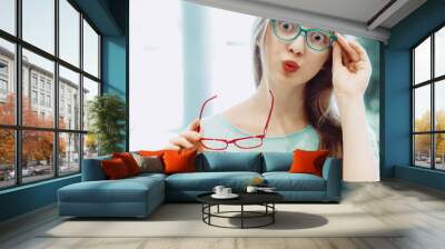 young woman trying on different pairs of eyeglasses Wall mural