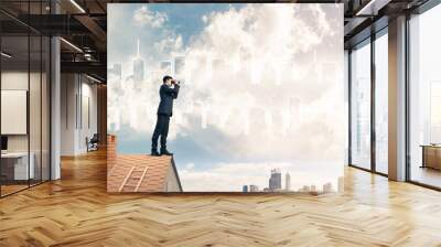 Businessman standing on roof and looking in binoculars. Mixed me Wall mural