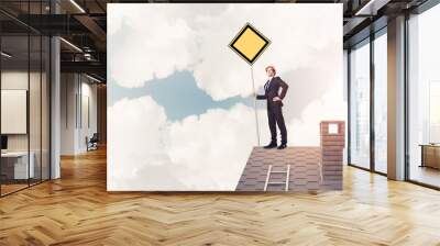 Young businessman on house brick roof holding yellow signboard.  Wall mural