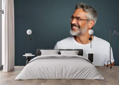 Retrato de un hombre latino maduro, con canas, sonriendo, con apariencia saludable y vitalidad, usando una camisa blanca y gafas, posando en un estudio fotográfico con fondo de color Wall mural