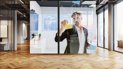 A focused executive organizes ideas using sticky notes on a glass wall in a bright, modern office, showcasing strategic thinking Wall mural