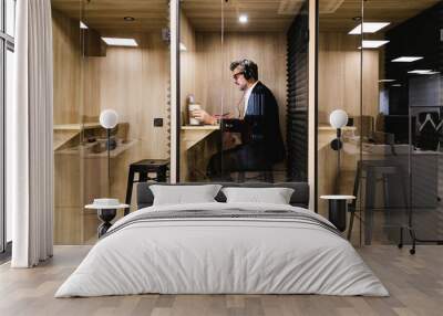 An executive engrossed in work uses headphones in a soundproof booth, ensuring privacy and concentration in a modern office Wall mural