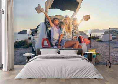 Mother with her two children in straw hats sitting in the trunk Wall mural