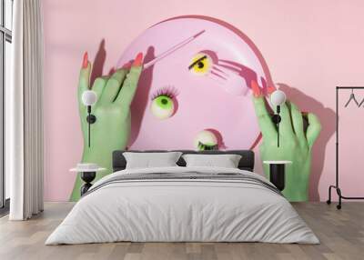 Creative layout with two green painted hands with fork and knife and green and yellow eyeball in pastel pink plate against pastel pink background. Halloween surreal idea.  Wall mural