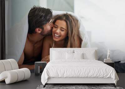 Those kisses that make you ridiculously happy. Shot of an affectionate young couple laying under a duvet together in bed. Wall mural