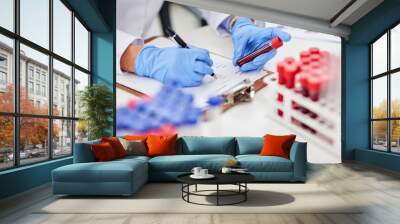 Compiling a detailed report of the latest findings. Closeup shot of a scientist examining a blood sample and recording findings in a lab. Wall mural