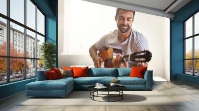 Honing his musical talent. Shot of a handsome young man playing a guitar at home. Wall mural