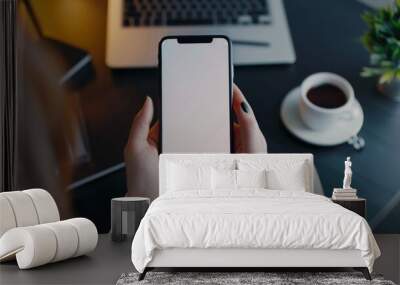 Mockup of Woman Holding Smartphone Over Desk in Modern Workspace with Blank Screen for Design Display Wall mural