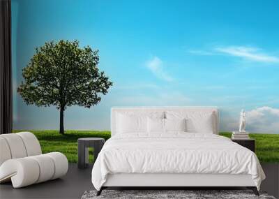 A single tree stands tall in a grassy field against a backdrop of a bright blue sky with white clouds. Wall mural