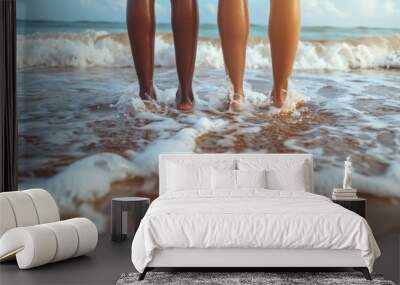 Rear back view of two women, female legs and barefoot feet standing on sand beach, sea or ocean water waves with foam splash Wall mural