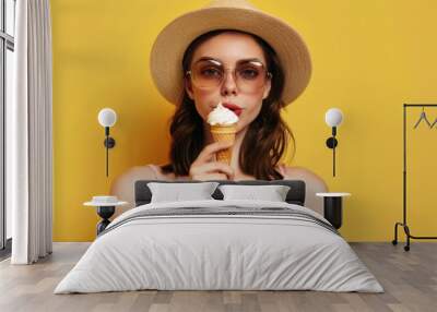 Stylish caucasian woman in hat and sunglasses with ice cream on yellow background Wall mural