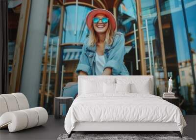 Woman leaving a hotel after a fun summer vacation. Happy female traveller smiling cheerfully while sitting on top of her lug Wall mural