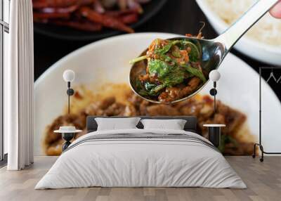 Focus Stir fried pork and basil on spoon and food on brown wooden table background. Favorite food in Thailand. Wall mural