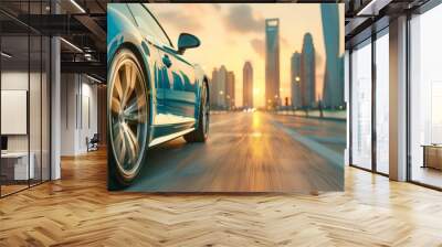 A blue sports car drives on a city road at sunset. The city skyline is in the background. Wall mural