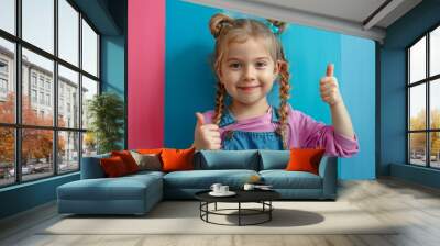 Smiling young girl with braided hair showing thumbs up gesture against a colorful background in casual outfit. Happy childhood concept. Wall mural