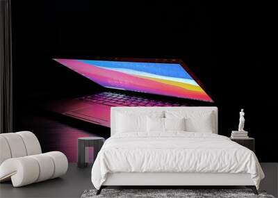 Laptop with half lid open on a table lit with colorful desktop screen wallpaper in a dark room	 Wall mural