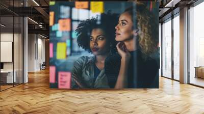 Two pensive businesswomen brainstorming ideas in a modern office interior with sticky notes on glass wall in the background Wall mural