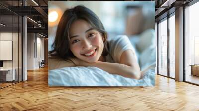 A beautiful Asian woman is smiling while lying on a bed. Wall mural