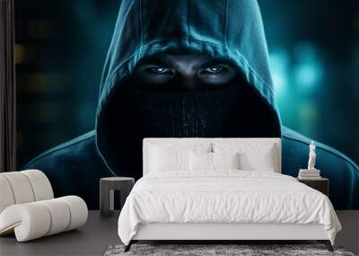 A masked man in a dark hoodie looking at the camera with blue eyes Wall mural