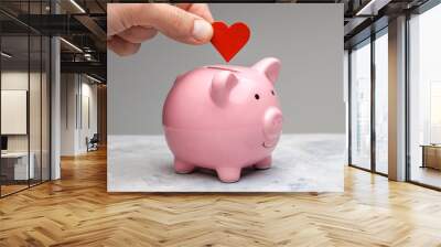 Donor. A man holds a red heart in his hand and goes to the piggy bank as a donation. Gray background Wall mural