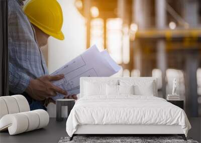 An engineer in a hard hat reviews blueprints at a construction site. Wall mural