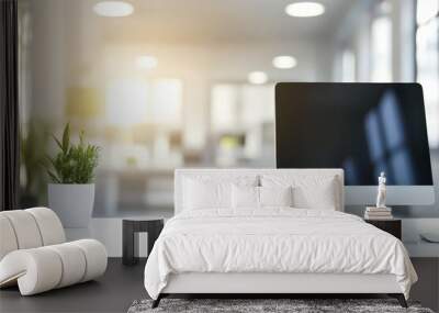 Close up of a white computer desktop with a monitor, keyboard and mouse with a potted plant in the foreground and a blurred office in the background. Wall mural