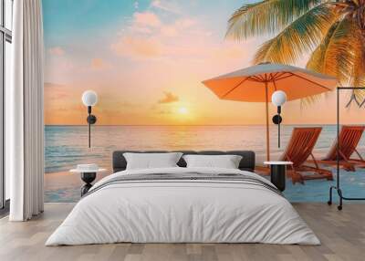 Two lounge chairs on a white sand beach under a palm tree with an umbrella, at sunset. Wall mural