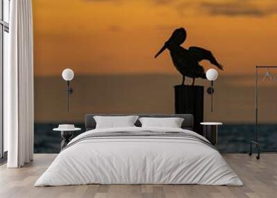 Pelican perched on a wooden post by the sea at sunset Wall mural